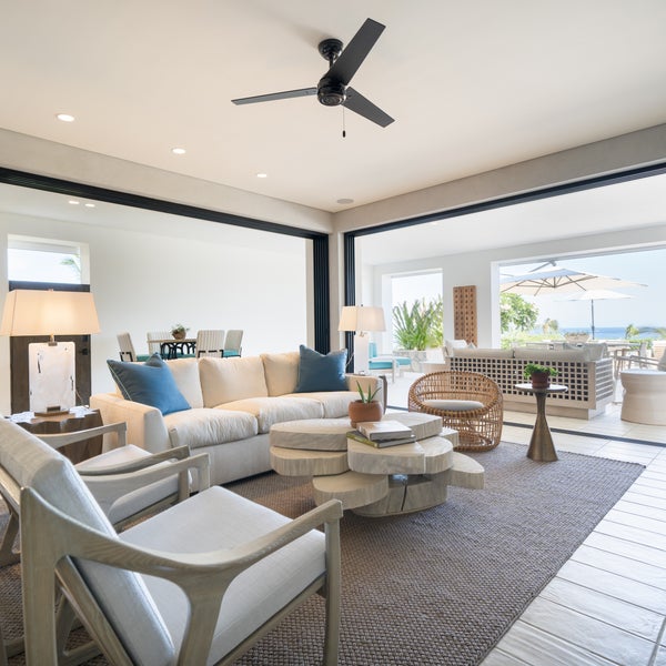 A large furnished room opens onto an outdoor patio with views of the ocean