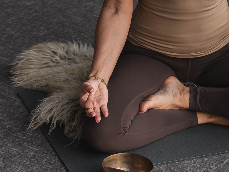 Person doing yoga next to a singing bowl and candles