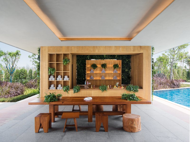 An outdoor spa like bar with a large rustic wooden table pictured center.  A pool sits to the right.