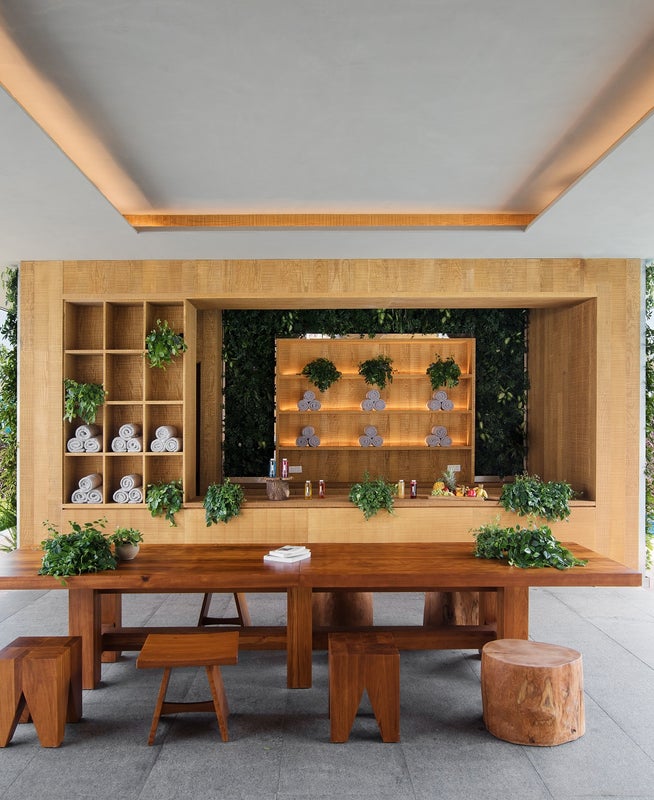 An outdoor spa like bar with a large rustic wooden table pictured center. A pool sits to the right.