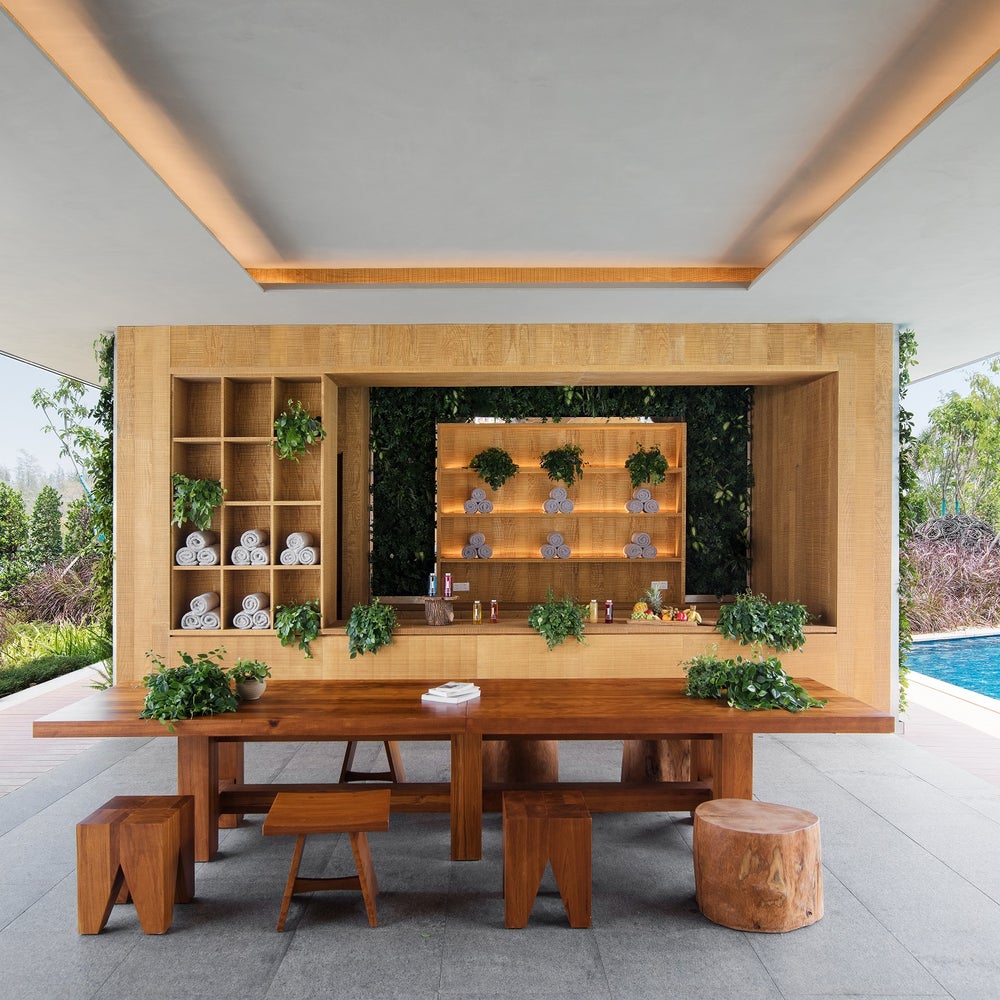 An outdoor spa like bar with a large rustic wooden table pictured center. A pool sits to the right.