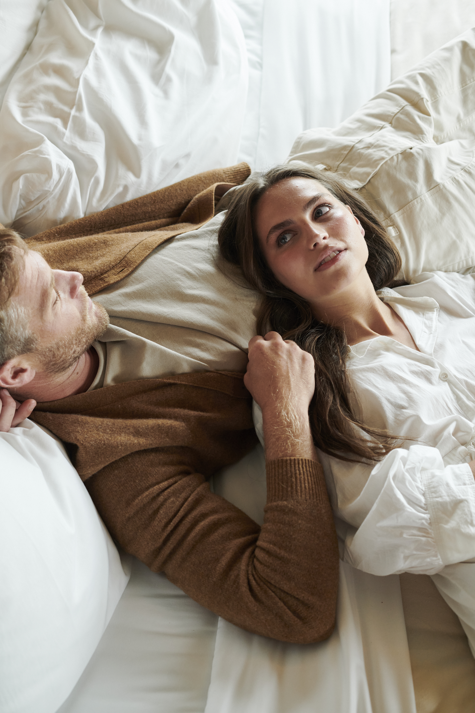A couple, one woman with her head laying on a man, rest together in a 1 Hotels bed
