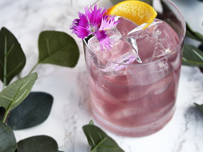 A pink cocktail with a lemon wedge and flower garnish