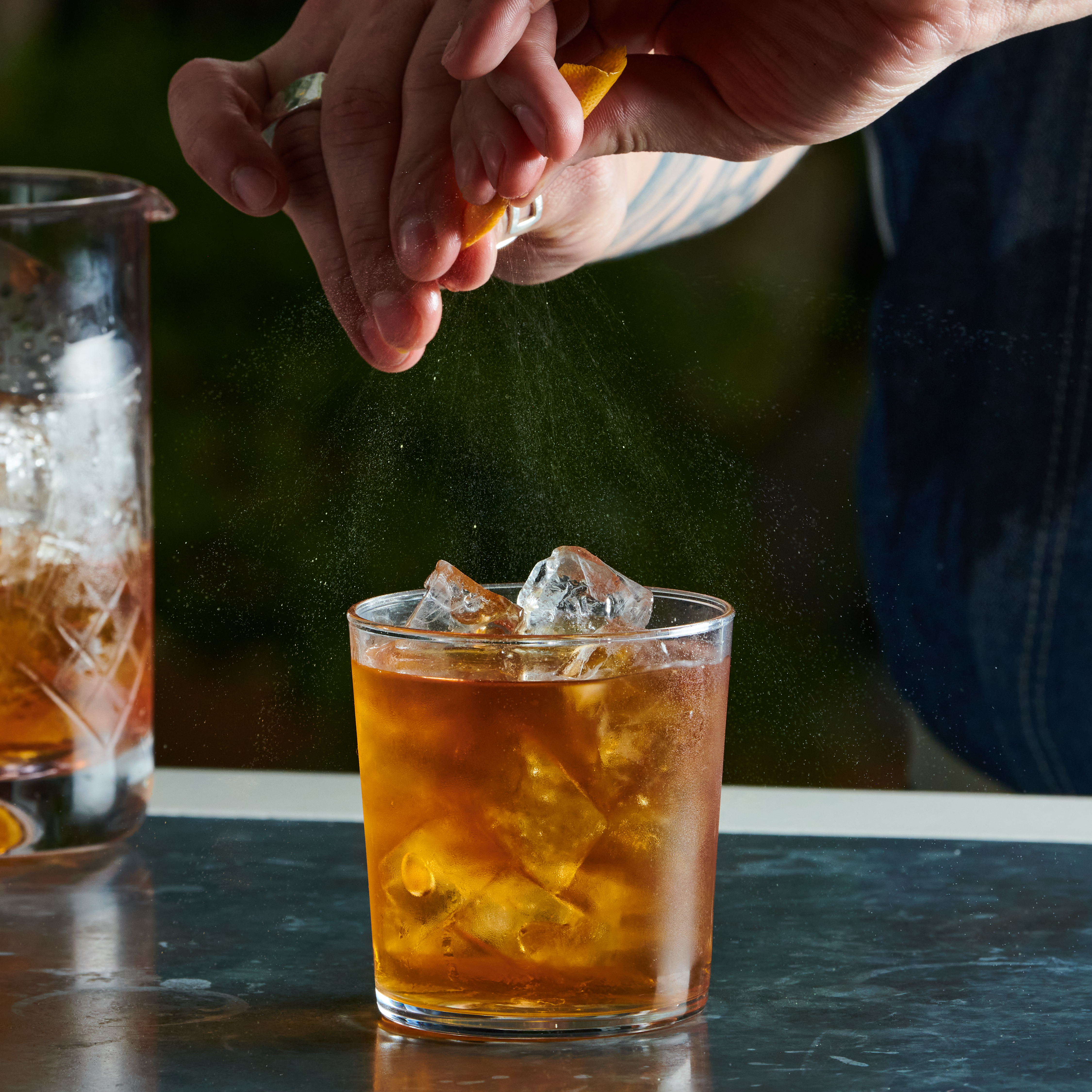 Person spritzing an orange twist over a negroni