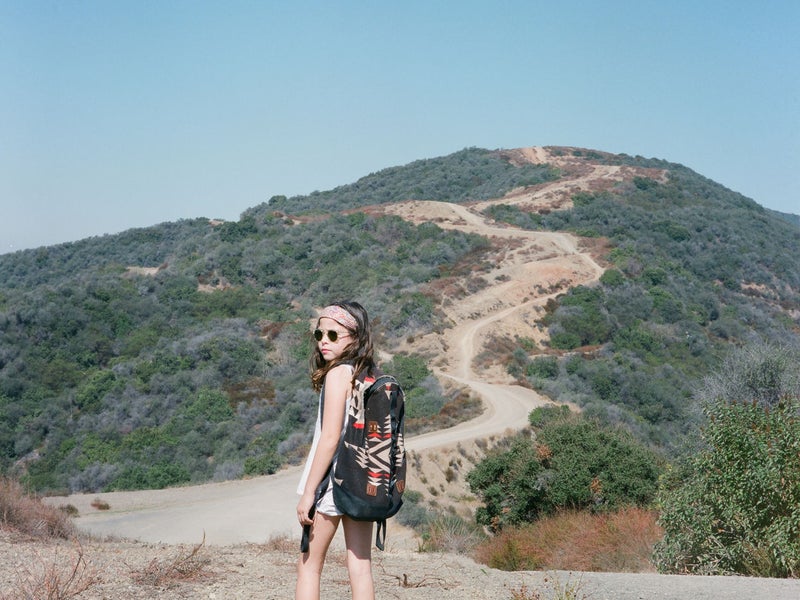 Child wearing a backpack and sunglasses on a hike