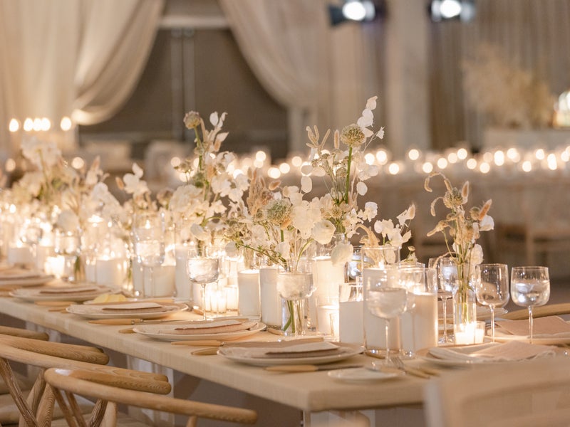 A beautifully set banquet table adorned with white flowers and glowing candles, creating a warm and elegant ambiance in a softly lit room