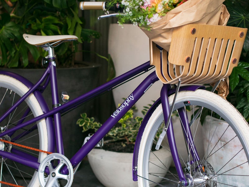 A purple bike with a bundle of flowers in the basket