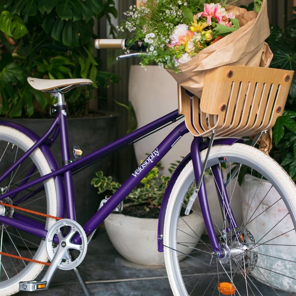 A purple bike with a bundle of flowers in the basket