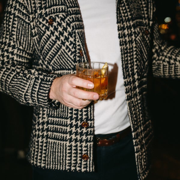 A man in a hounds tooth patterned blazer holds a cocktail