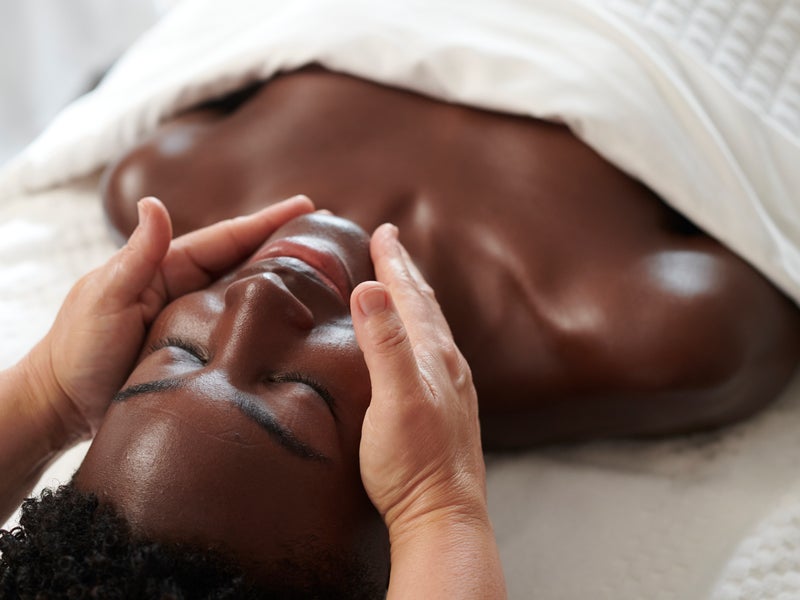 A woman lying face up on a massage bed receives a relaxing spa facial