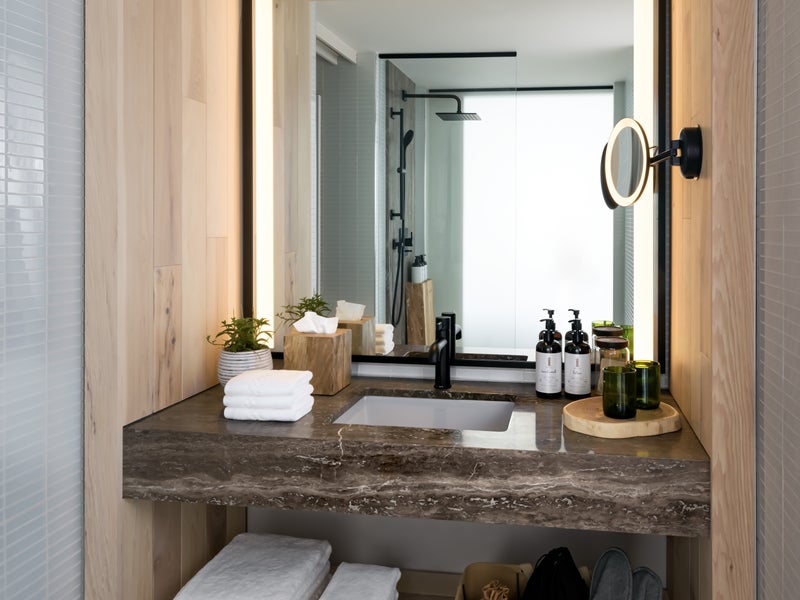 A bathroom sink with folded linen, granite countertop and backlit vanity mirror