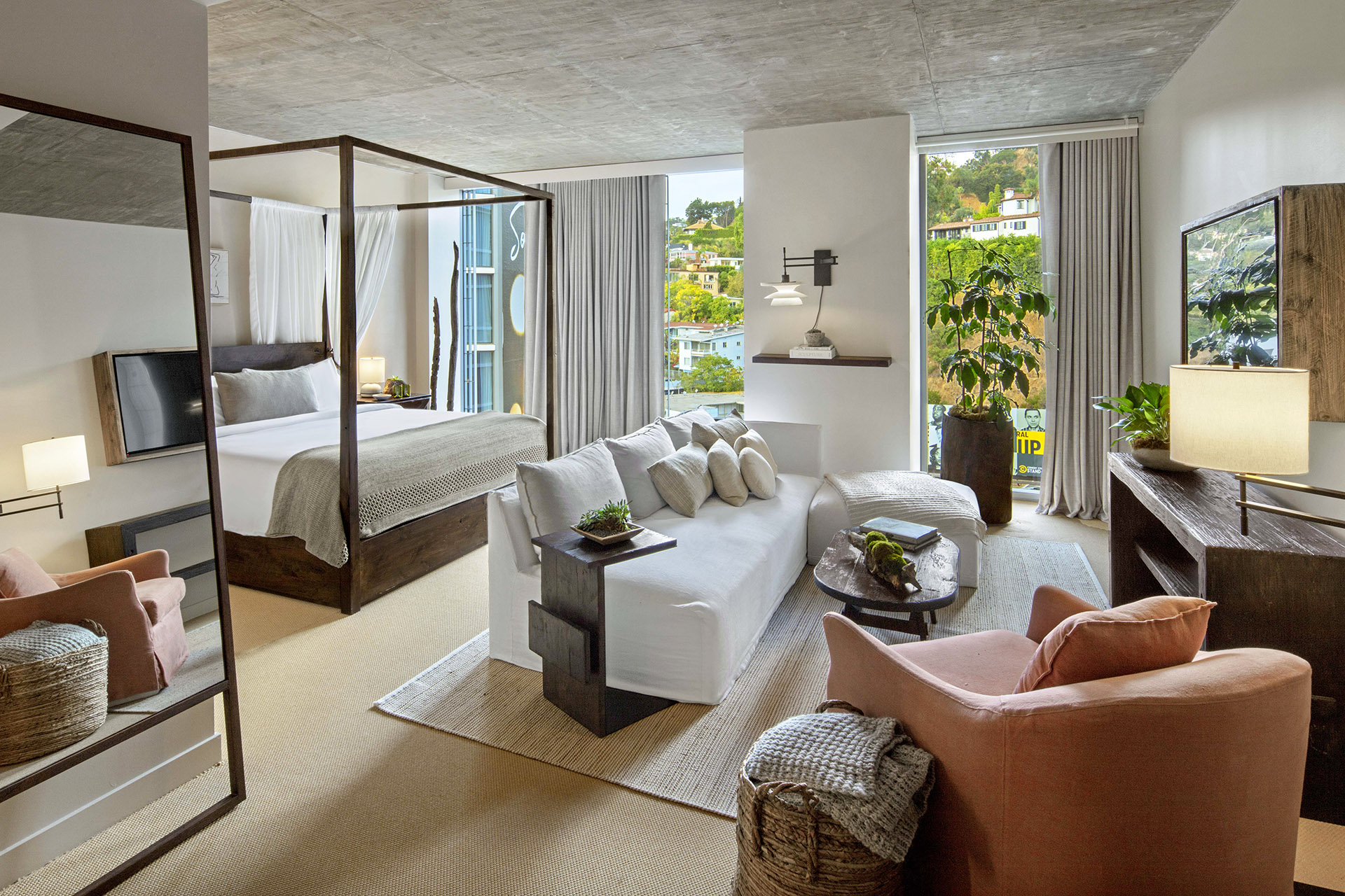 A king size bed sits under a canopy frame.  A white sofa is positioned in front of the bed facing a television.