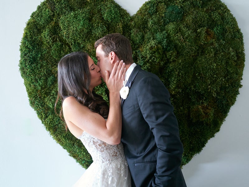 Two people kissing in front of a moss heart
