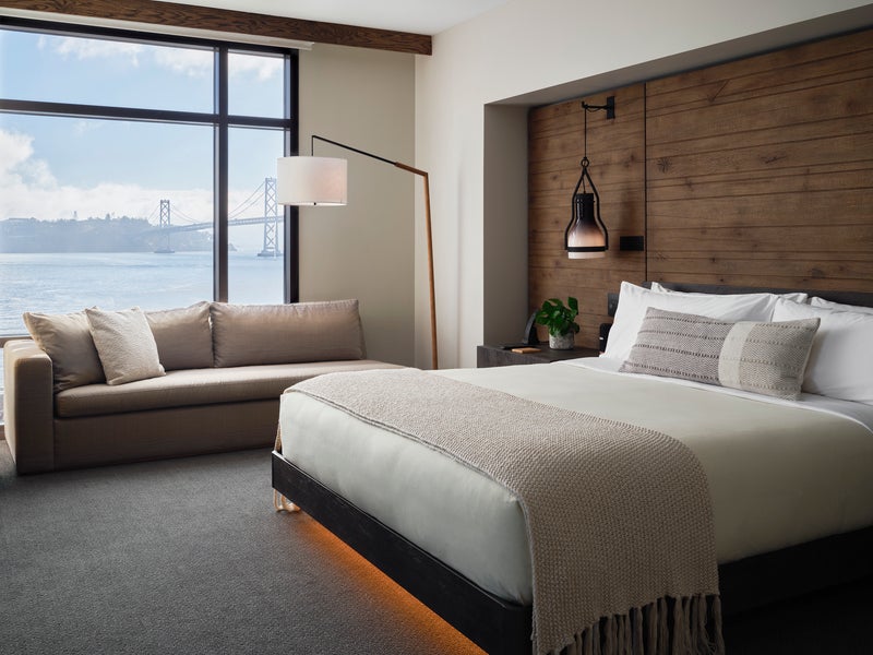 A king size bed sits center of the room, while a sofa sits positioned against a window overlooking the water