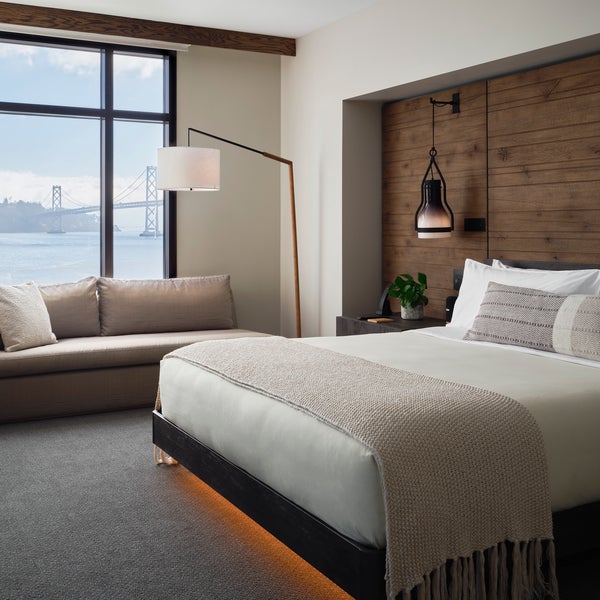 A king size bed sits center of the room, while a sofa sits positioned against a window overlooking the water
