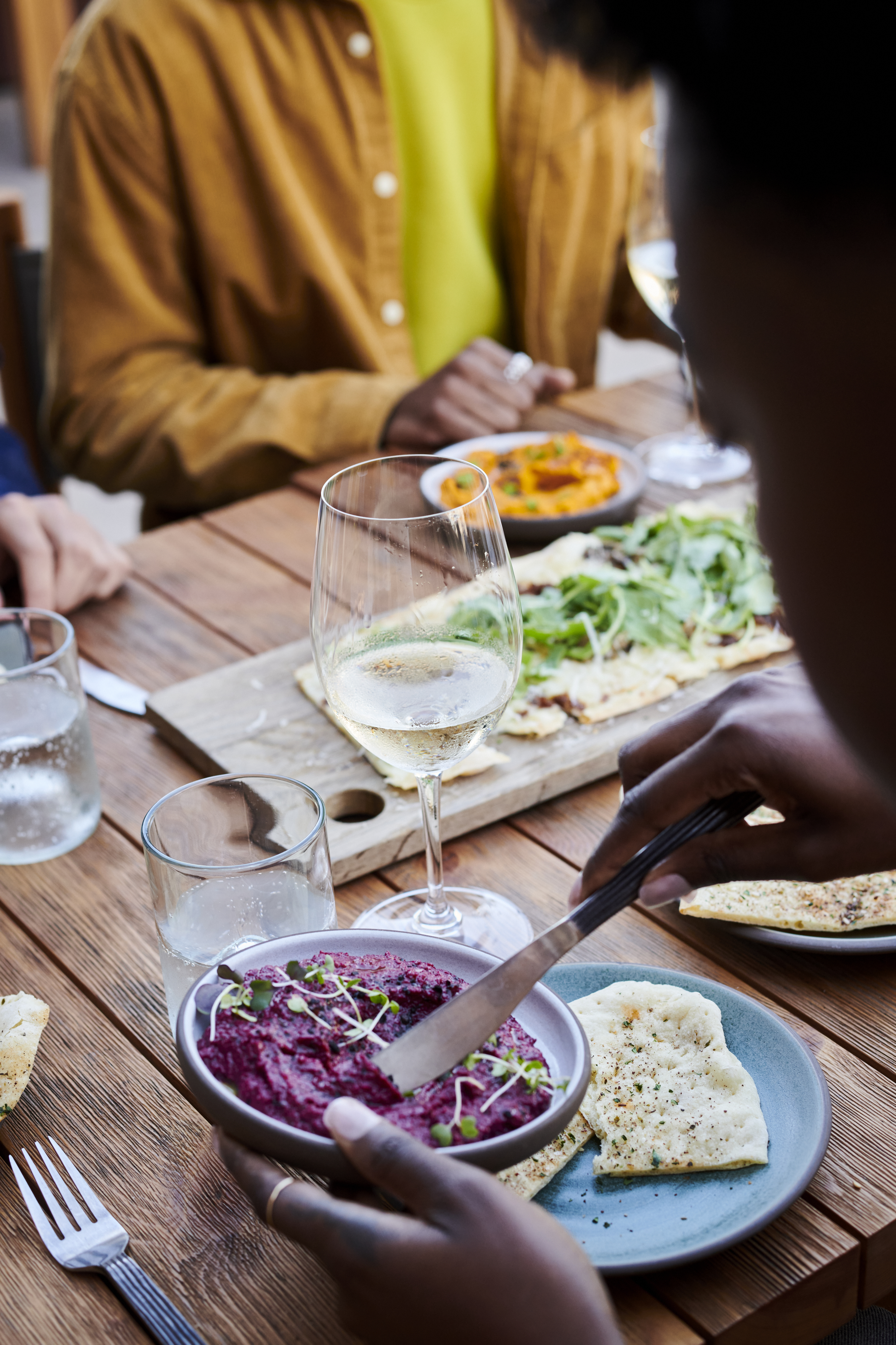 Persone sedute attorno a un tavolo di legno assaggiano una varietà di salsine con pane pita