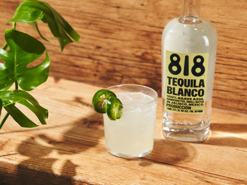 Margarita with jalapeno garnish next to a bottle of 818 tequila