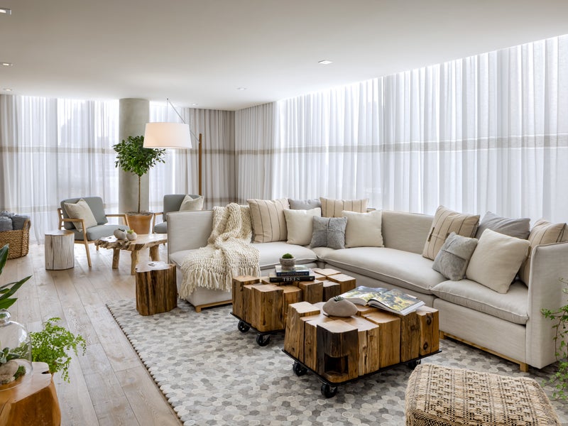 A 1 Hotel guestroom featuring a large white sectional, wooden coffee tables, and green accent plants