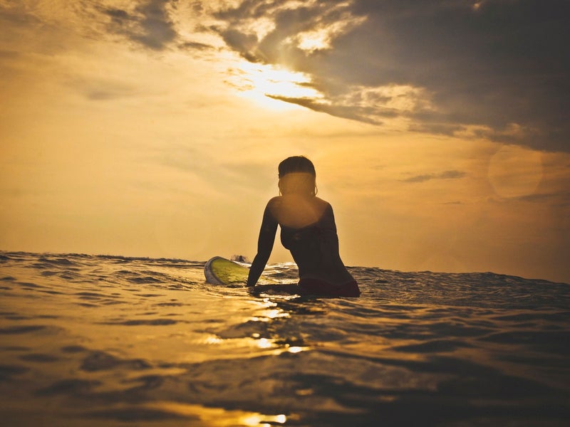 surfer sitting on their board in the water at sunrise