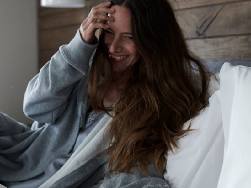 A woman wearing a gray robe gets cozy in bed