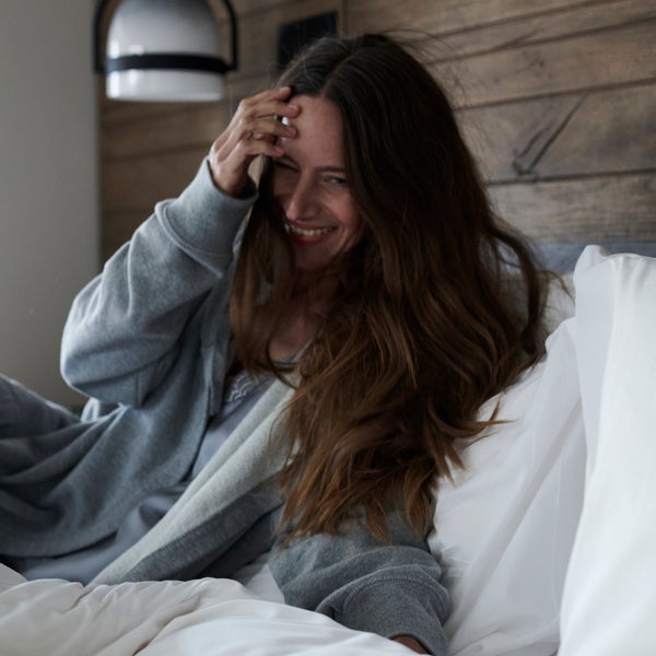 A woman wearing a gray robe gets cozy in bed
