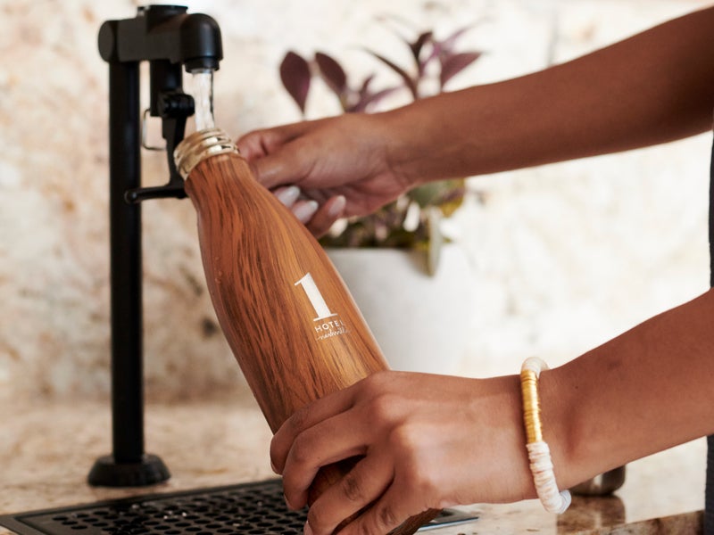 Person filling a wood grain 1 Hotels branded water bottle at a tap