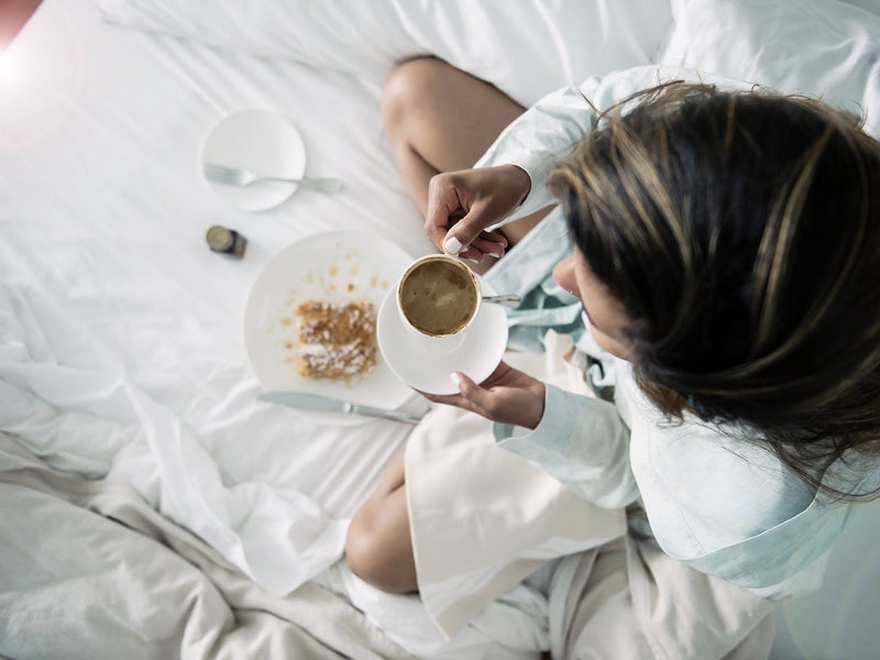 Person in a robe sitting on a bed holding a mug