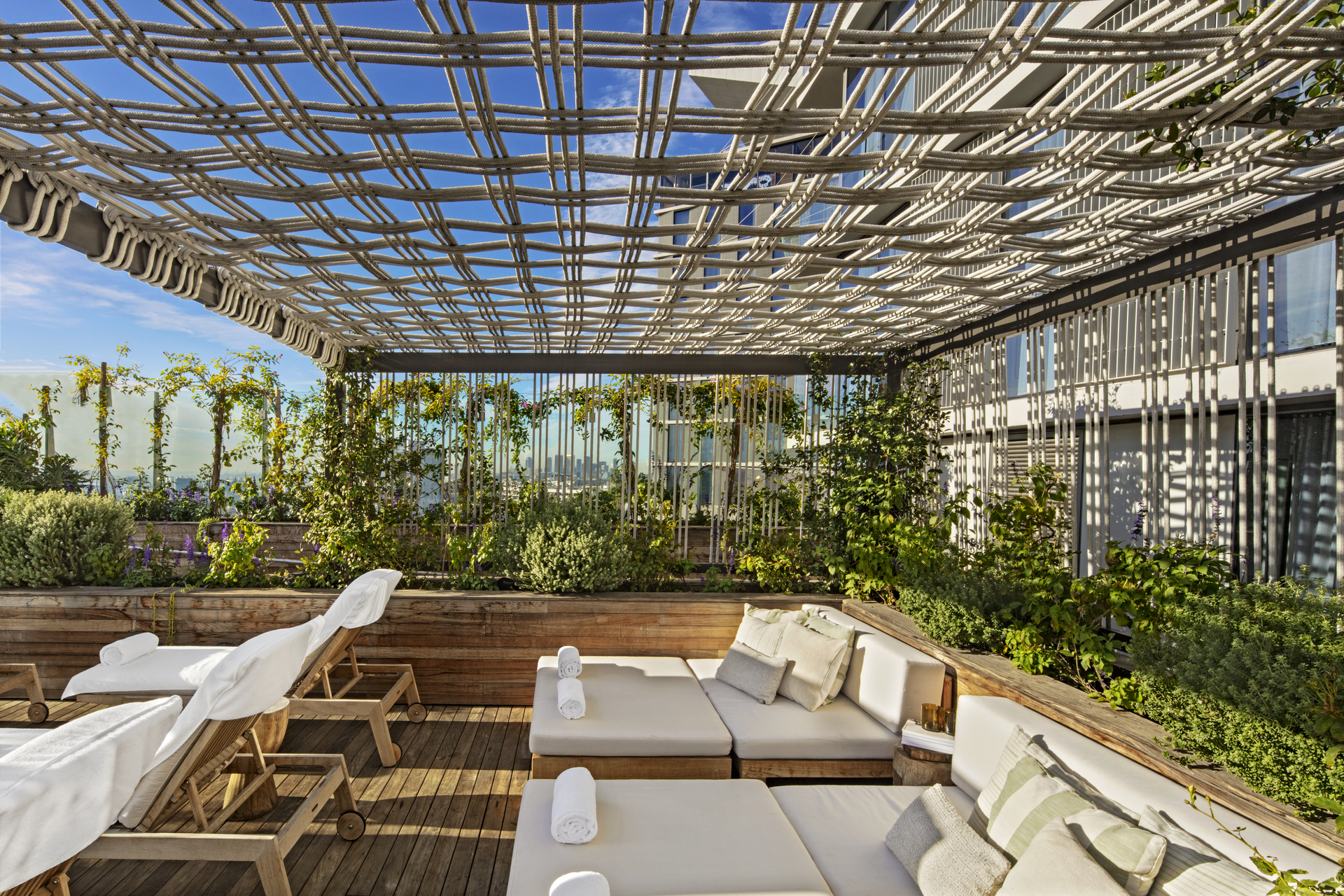 A rooftop lounge area with reclined lounge chairs is featured within a wall of green plant life
