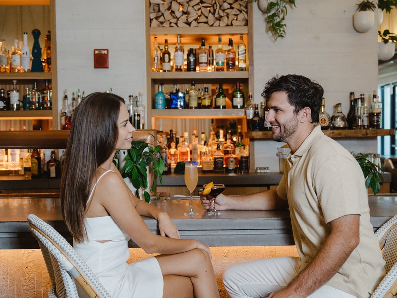 Two people sitting at a bar with cocktails