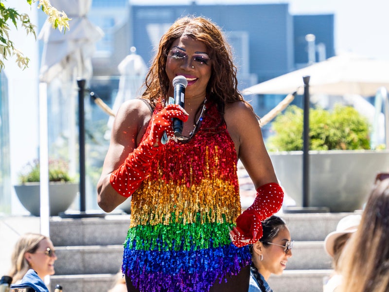 Person wearing a rainbow bead dress with red gloves speaking into a microphone