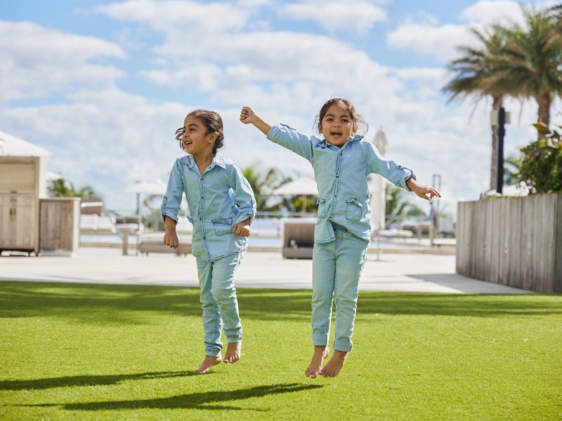 Two small children in matching denim outfits jumping and smiling for the camera