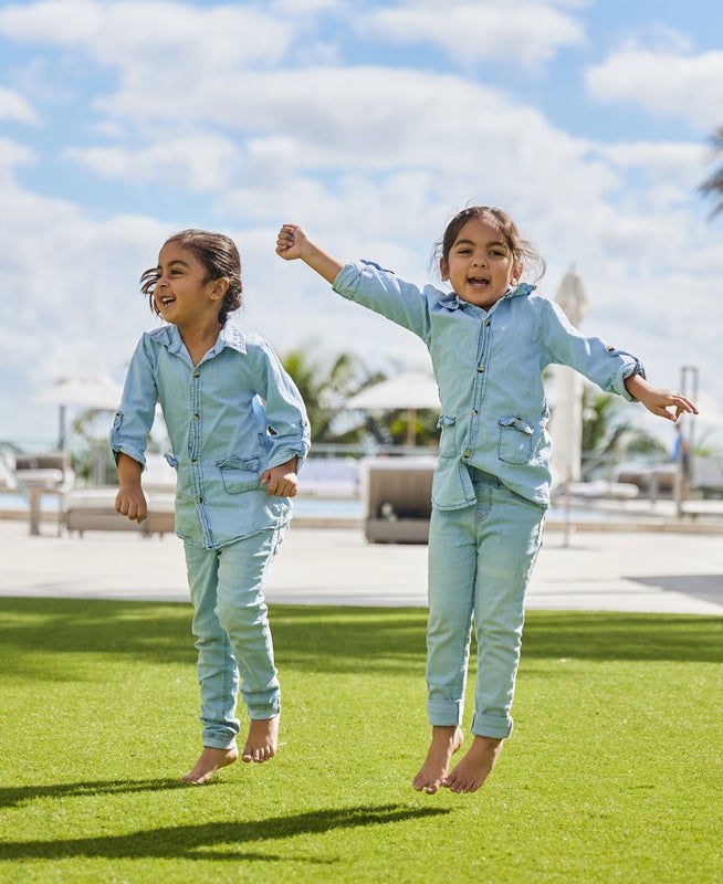 Two small children in matching denim outfits jumping and smiling for the camera