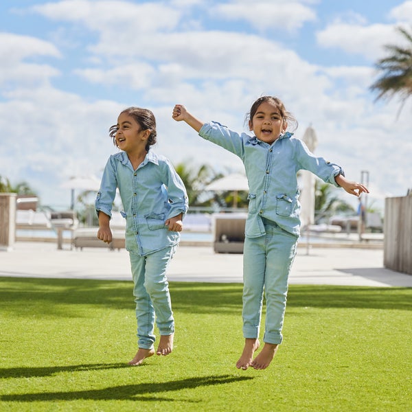 Two small children in matching denim outfits jumping and smiling for the camera