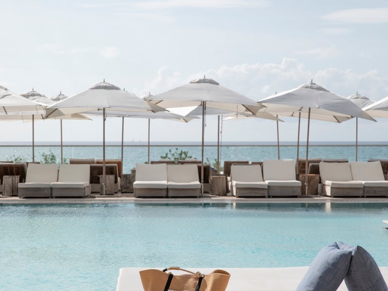 A white mattress and a Rothy's bag are placed on the edge of a pool, creating a serene outdoor setting.