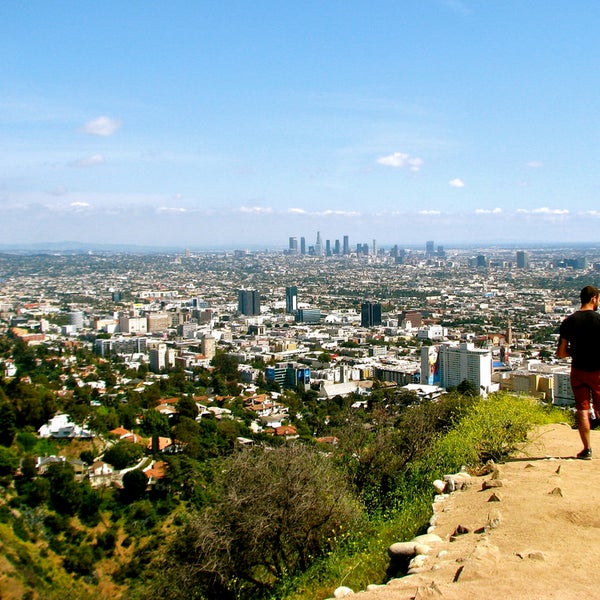 A man in athleisure stands overlooking the canyon, nearest, and city scape, further in the distance