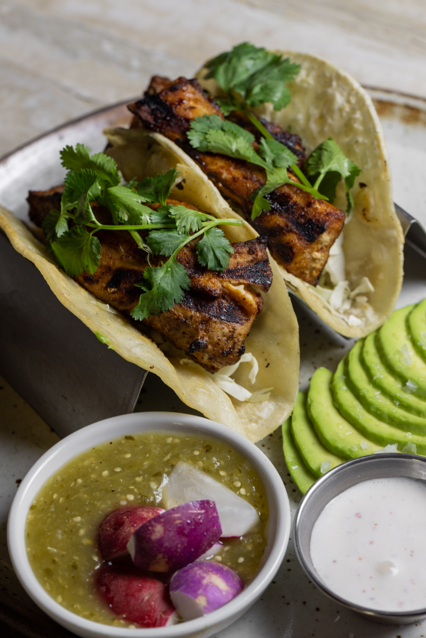 Two tacos with a green sauce on the side