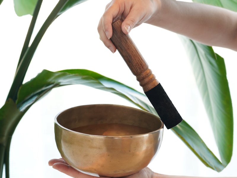 A hand holding a singing bowl, while another hand runs the mallet along the edge