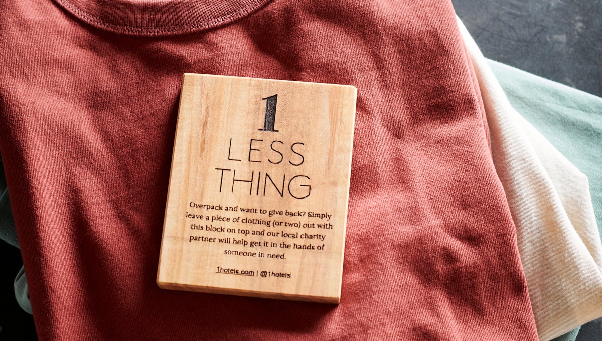 A wooden block captioned One Less Thing sits atop a red folded shirt