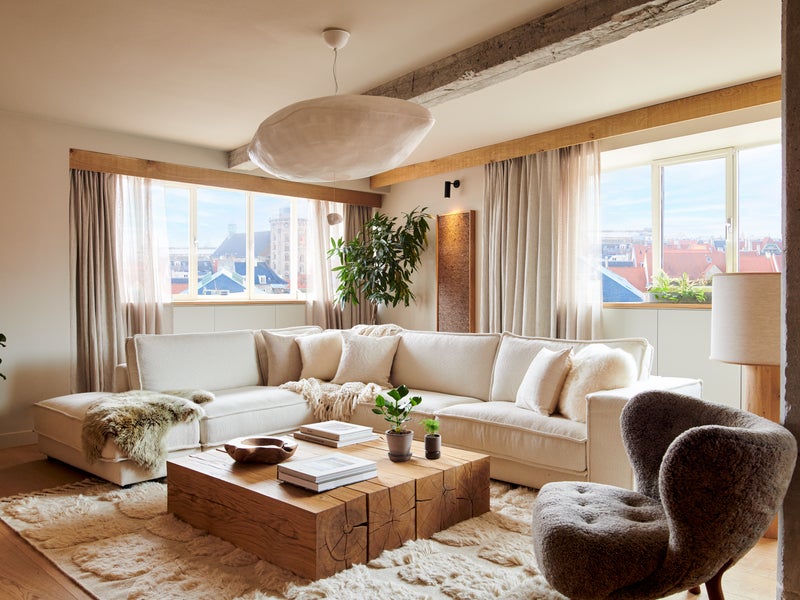 A well-appointed living room with two large windows, an area rug and coffee table, a sectional and arm chair