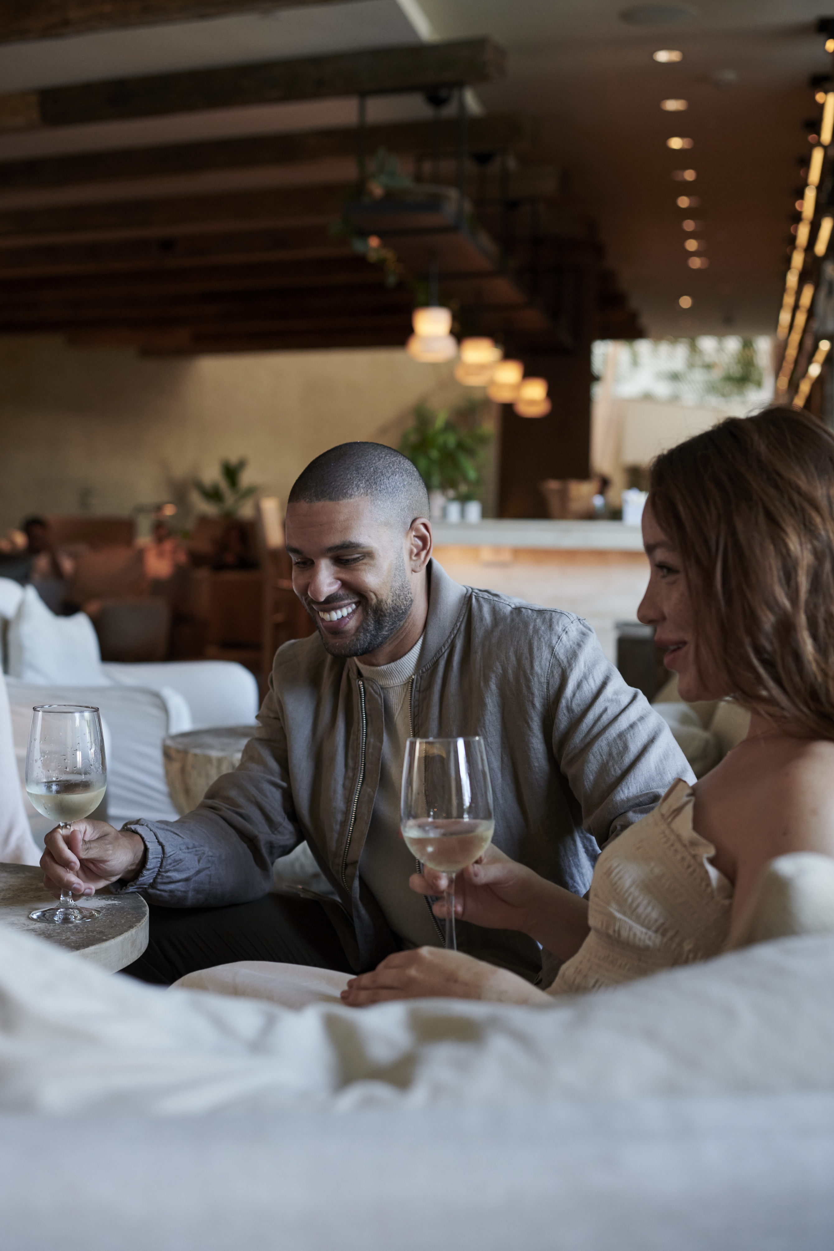 A man and woman laugh while holding their wine glasses in front of them