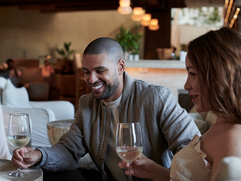 A man and woman laugh while holding their wine glasses in front of them