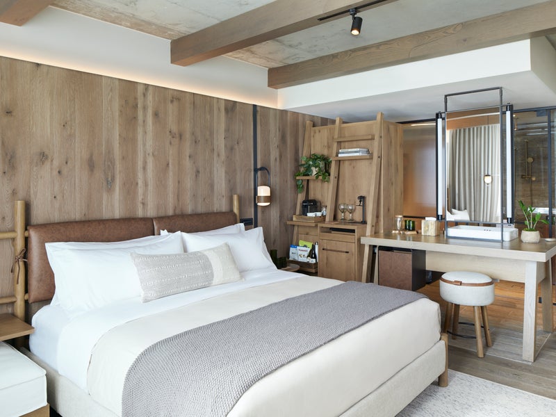 A king sized bed sits to the left of a small kitchenette area.  A vanity mirror sits atop a desk to the right of the kitchenette