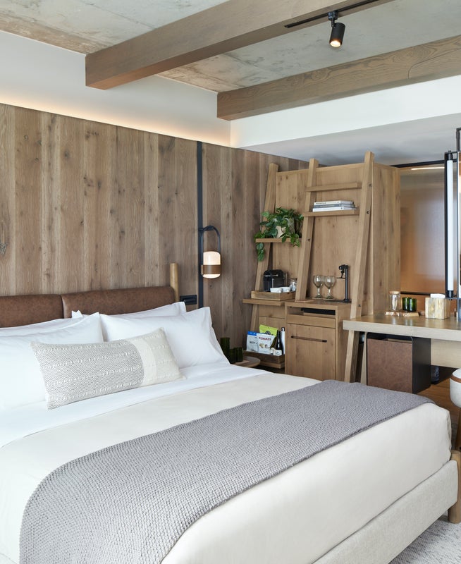 A king sized bed sits to the left of a small kitchenette area.  A vanity mirror sits atop a desk to the right of the kitchenette
