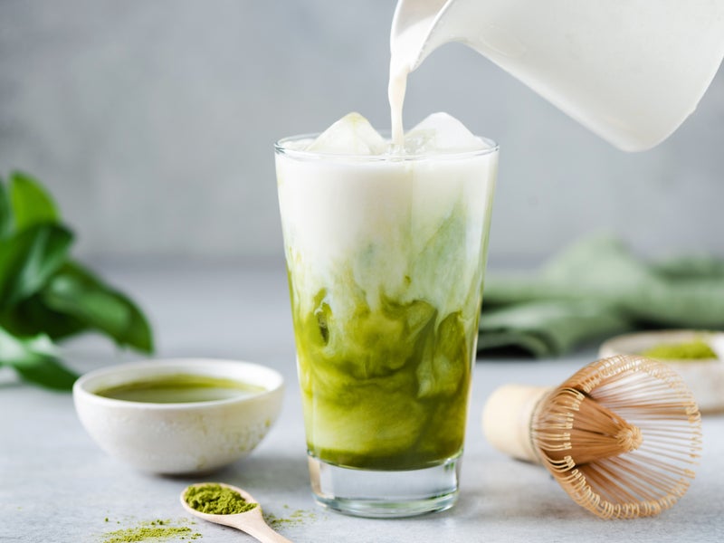 A glass of iced matcha with milk being poured in