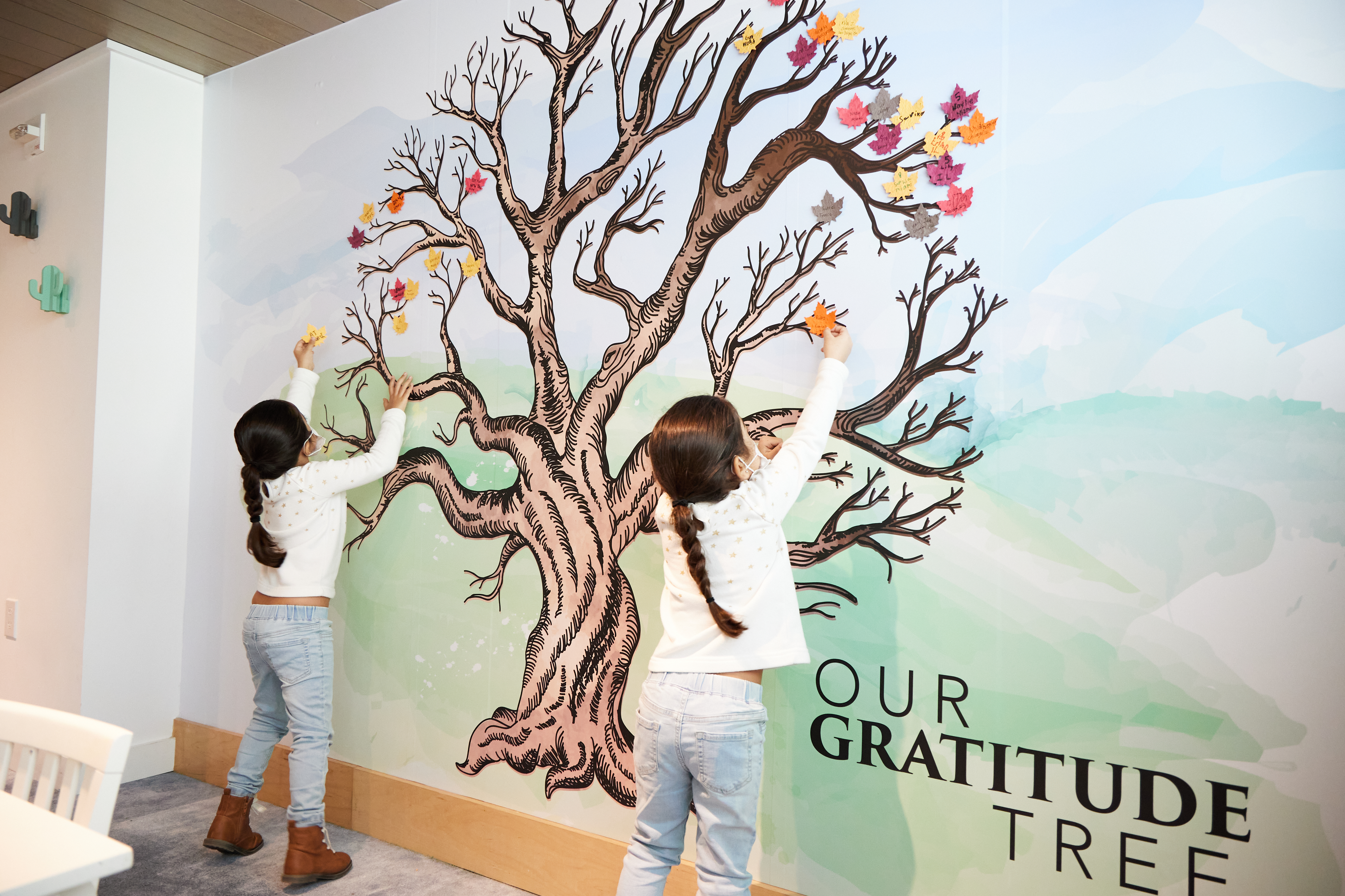 Two children putting leaves on a tree painting