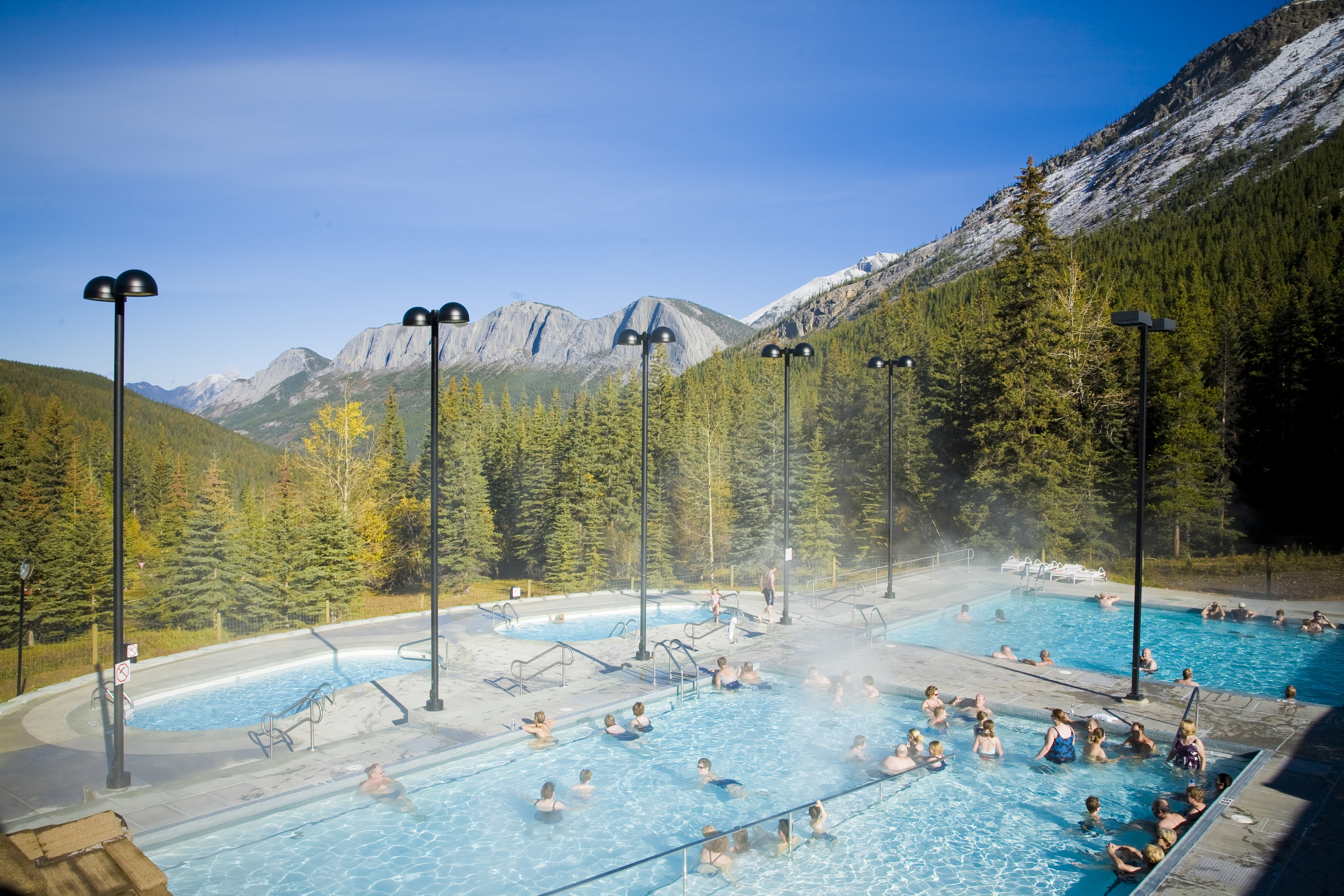 People in outdoor hot spring pool with a view of mountains and dense forest on a bright day