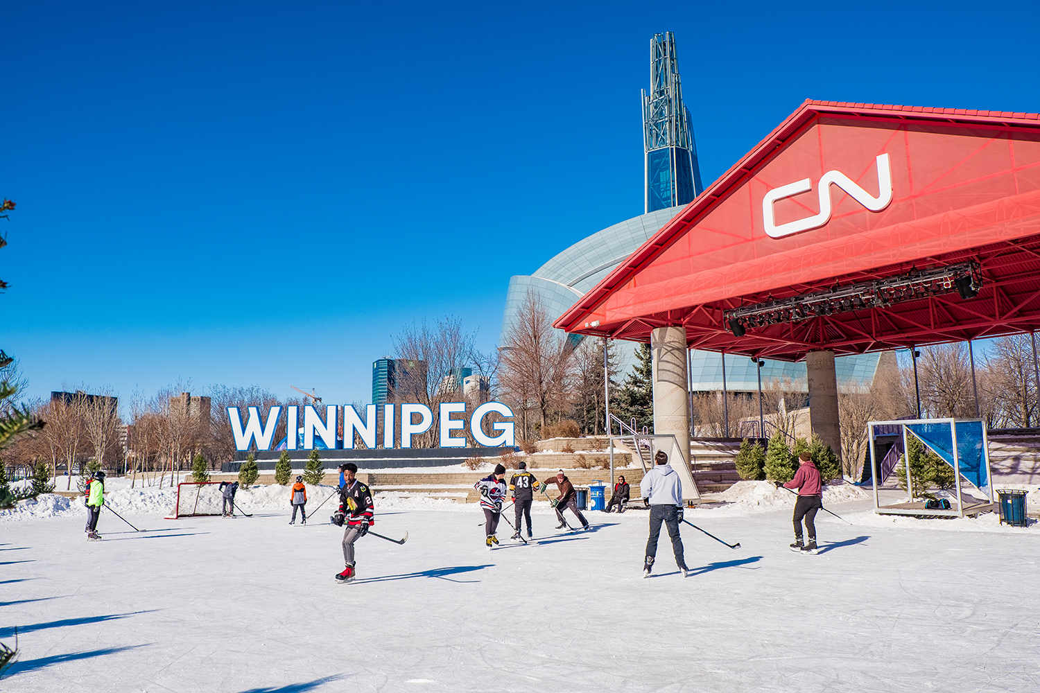 People playing ice hockey on an outdoor ice rink by the CN stage and Winnipeg sign
