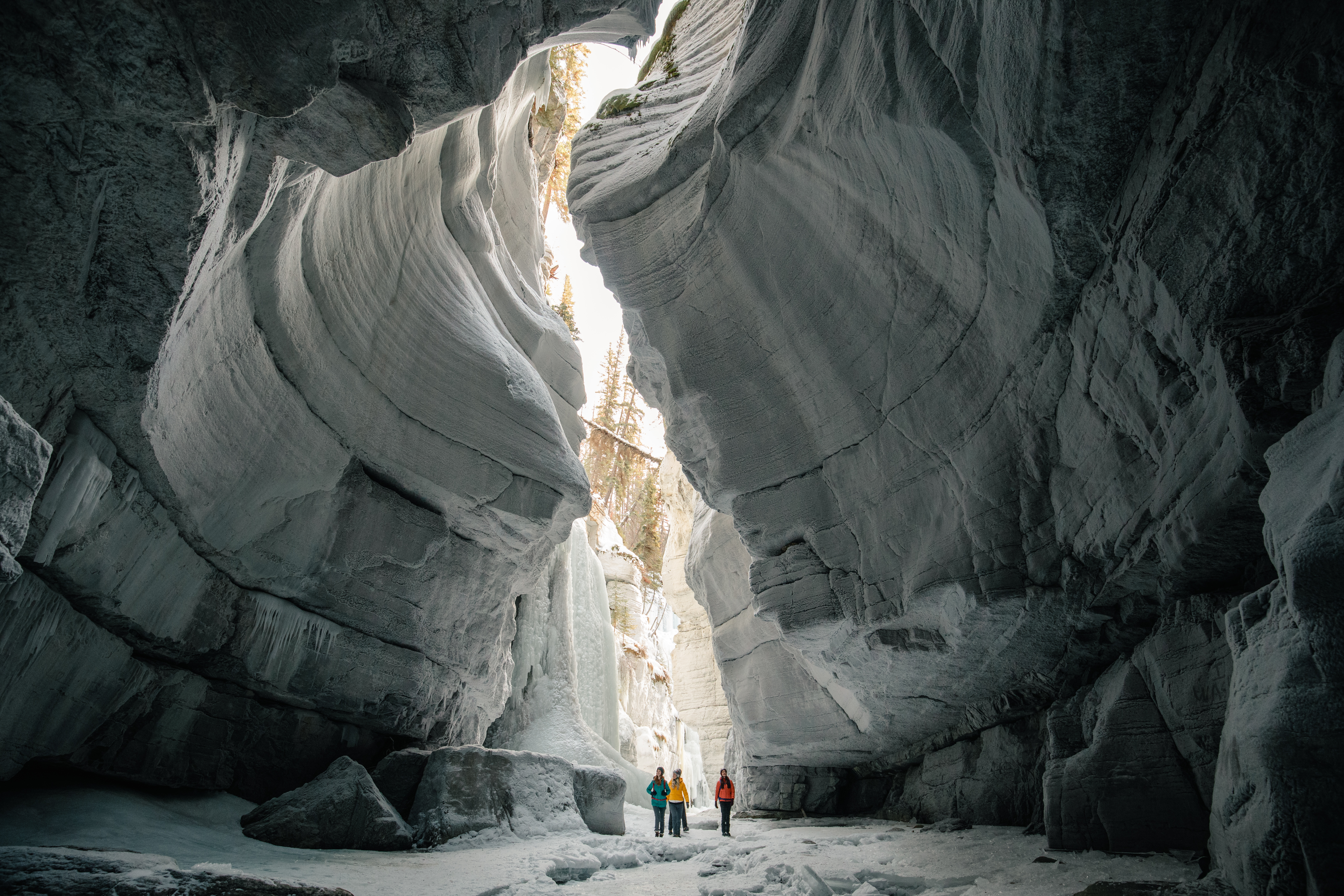 Three people standing in an icy canyon cave