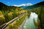 Rocky Mountaineer rides along river and forestry with Canadian Rockies in the background during fall