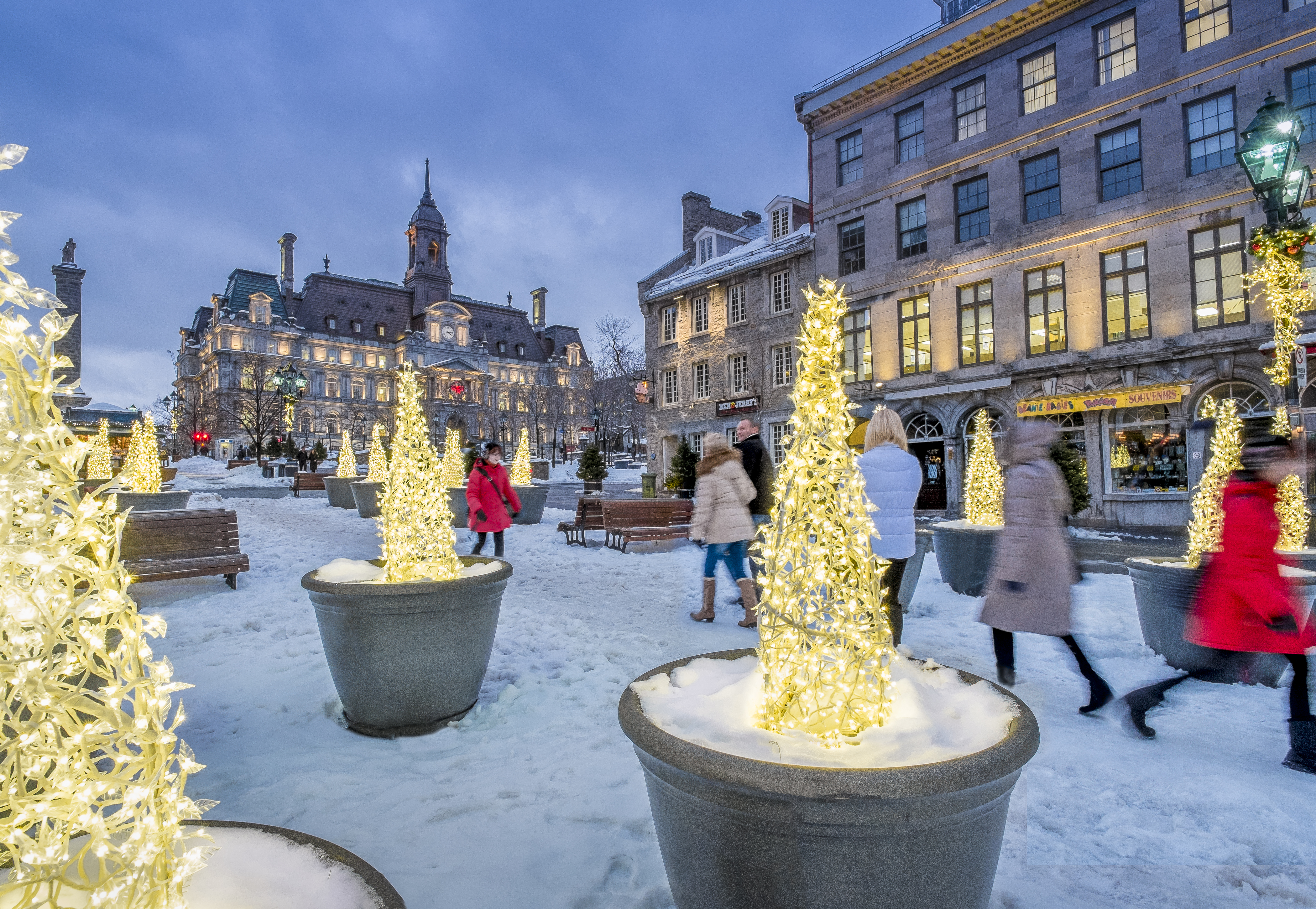 People walk through a snowy square in Old Montreal with bright lights and old buildings all around
